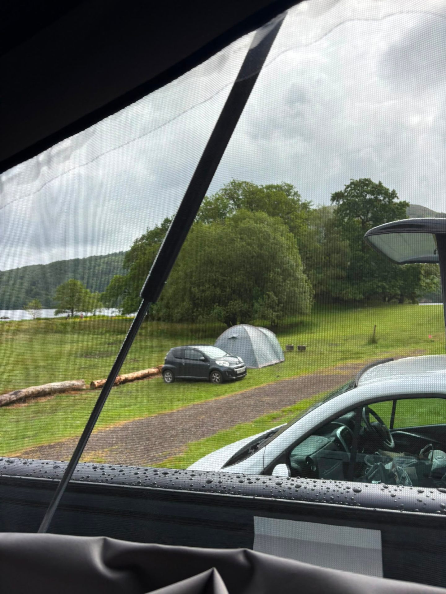 View through the campervan window of a tent and lake beyond